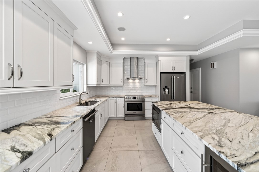 Kitchen with white cabinets, black appliances, a raised ceiling, light stone countertops, and a kitchen island