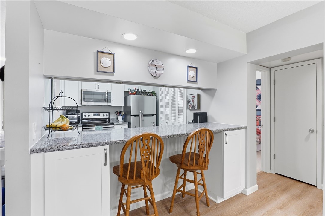 Kitchen featuring white cabinets, light stone counters, stainless steel appliances, light wood-style flooring, and a breakfast bar