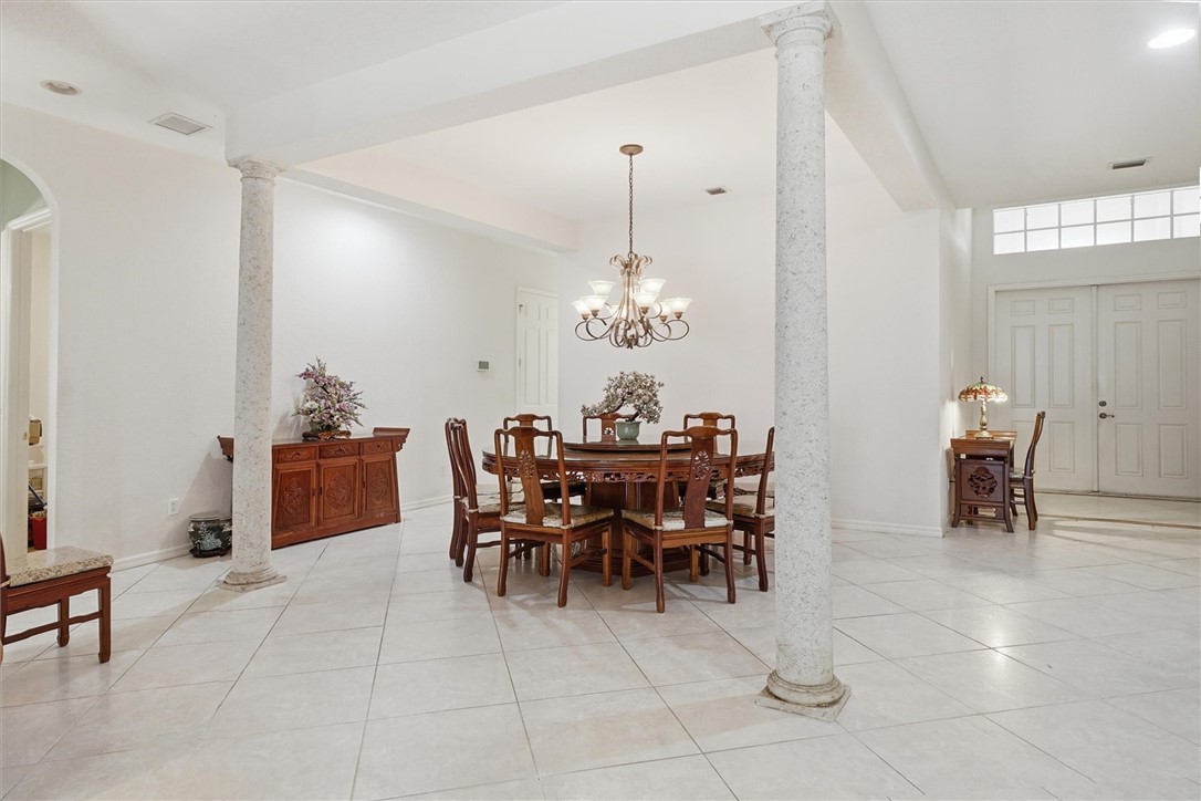 Spacious open-concept interior featuring light-toned tile flooring, architectural columns, a decorative chandelier, and double entry doors with a transom window