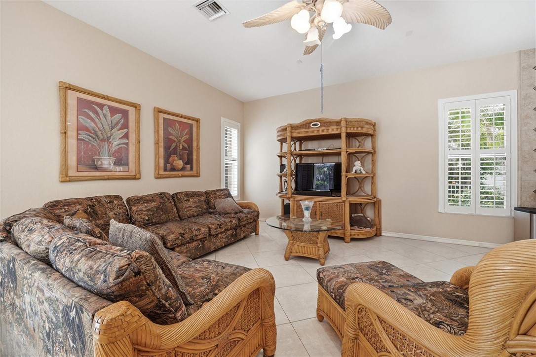 Spacious living area featuring light-toned tile flooring, vaulted ceilings, and a ceiling fan with integrated lighting