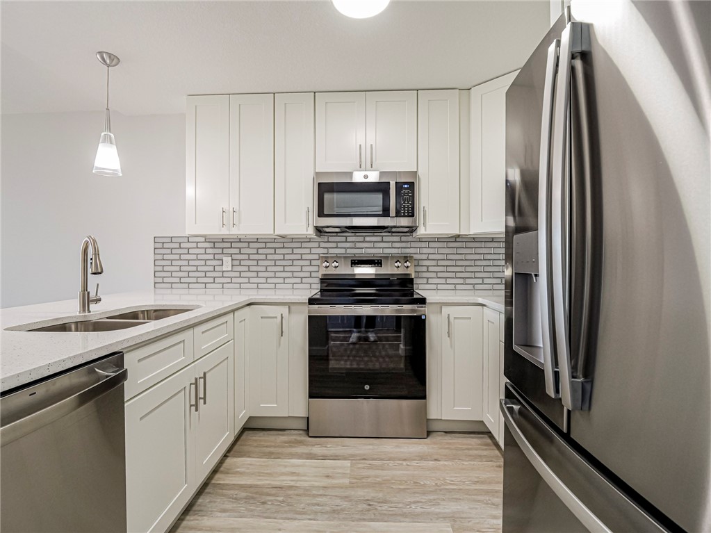 Kitchen with GE stainless steel appliances, white cabinetry, light quartz counters, hanging light fixtures, and decorative backsplash
