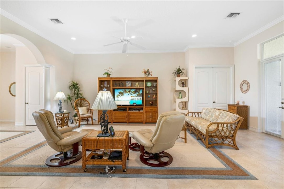 Living room featuring arched walkways, light tile patterned flooring, ornamental molding, a ceiling fan, and recessed lighting