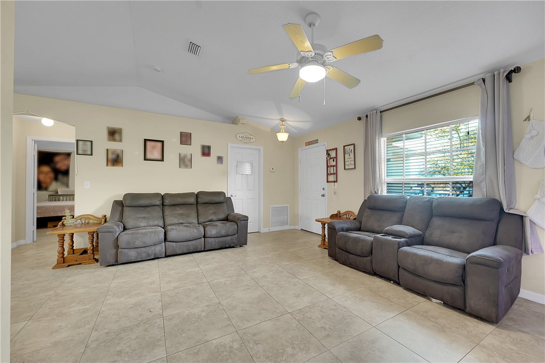 Living area with lofted ceiling, light tile patterned floors, and ceiling fan