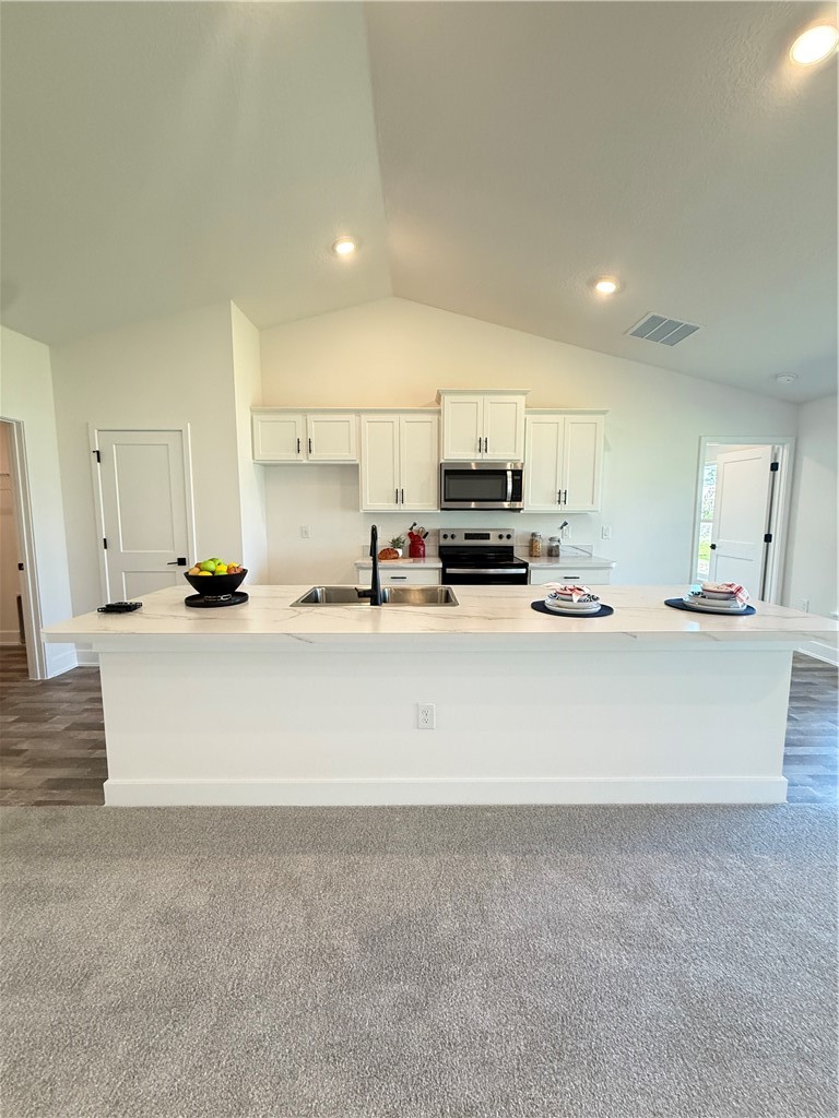Kitchen featuring white cabinetry, stainless steel electric range, a large island, lofted ceiling, and dark colored carpet