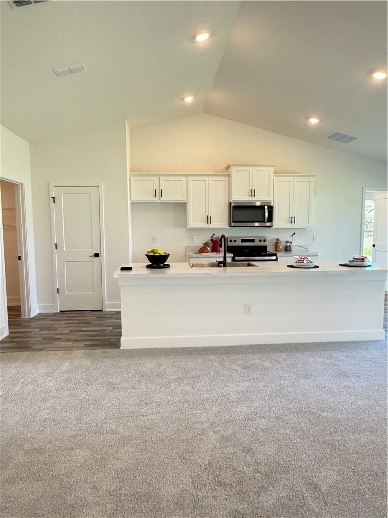 Kitchen featuring white cabinetry, a kitchen island with sink, stove, lofted ceiling