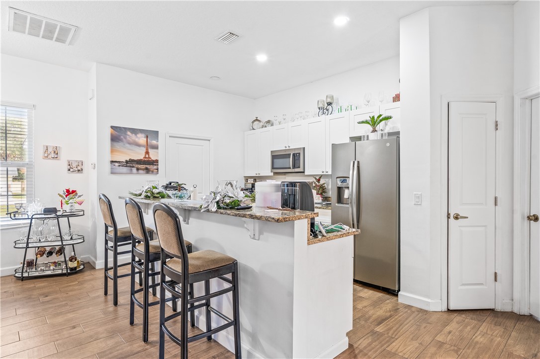 Kitchen with a breakfast bar, dark stone countertops, stainless steel appliances, light wood-style flooring, and white cabinetry