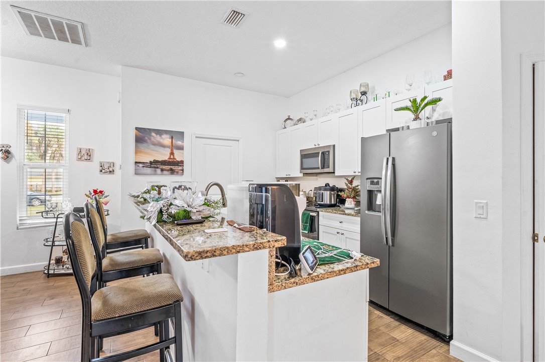 Kitchen with light stone counters, stainless steel appliances, white cabinets, a kitchen breakfast bar, and a center island with sink