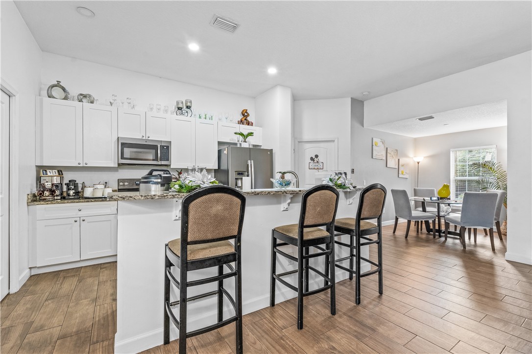 Kitchen featuring a kitchen bar, light stone counters, white cabinets, dark wood-type flooring, and recessed lighting