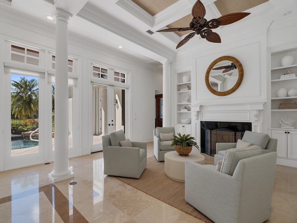 Living room featuring decorative columns, crown molding, a fireplace, built in shelves, and french doors