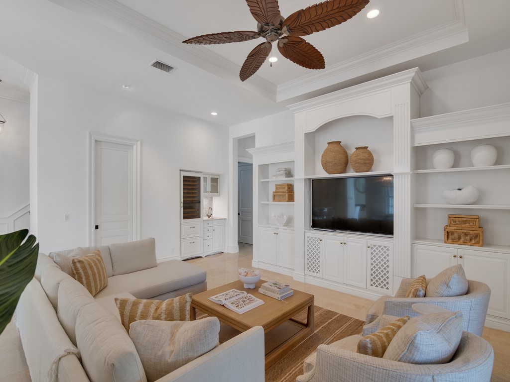 Living room with ornamental molding, ceiling fan, recessed lighting, built in features, and a raised ceiling