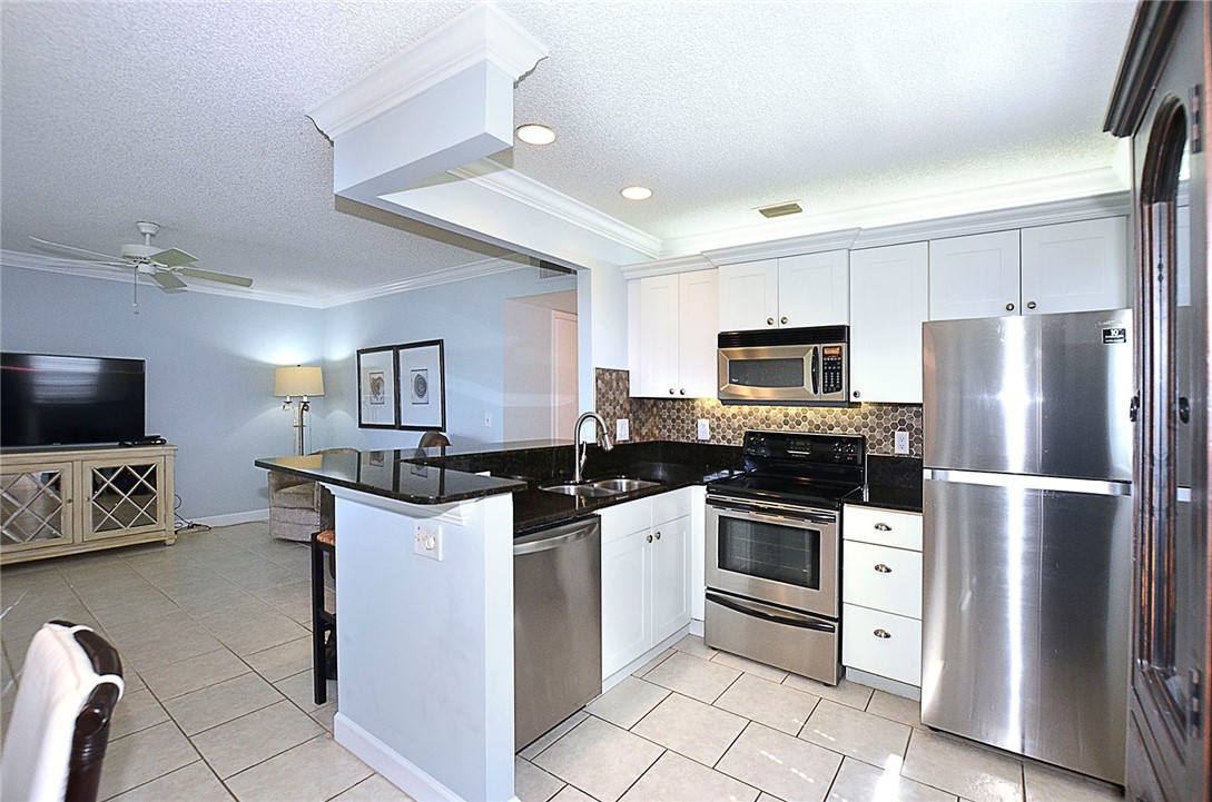 Kitchen featuring a textured ceiling, appliances with stainless steel finishes, crown molding, decorative backsplash, and dark stone counters