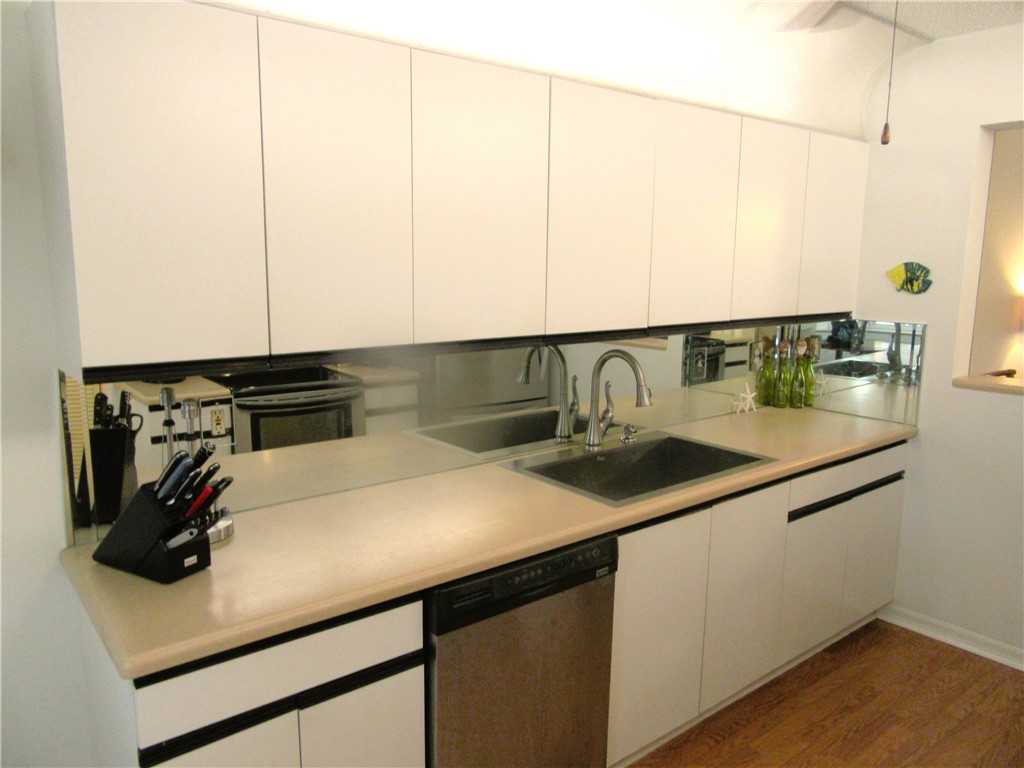 Kitchen featuring light countertops, dark wood finished floors, stainless steel dishwasher, and white cabinets