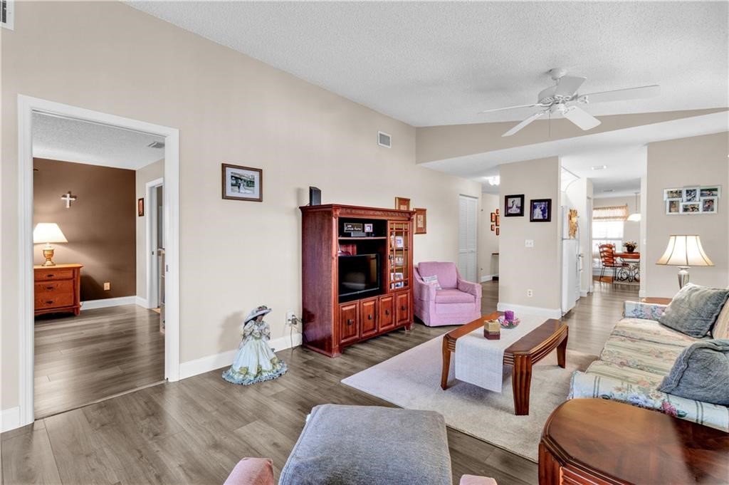 Living room with wood finished floors, a textured ceiling, a ceiling fan, and lofted ceiling