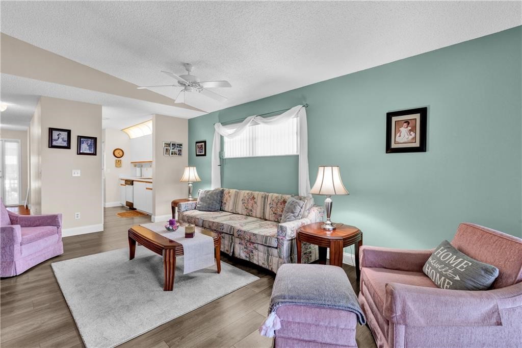 Living area featuring a textured ceiling, wood finished floors, ceiling fan, and healthy amount of natural light