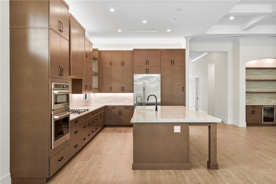 Kitchen with ornamental molding, light wood-type flooring, a center island with sink, light stone counters, and backsplash