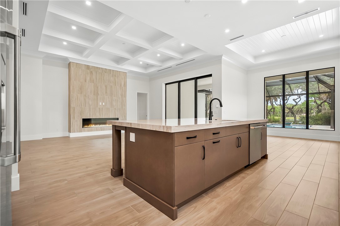 Kitchen with a spacious island, a tiled fireplace, light wood-style floors, coffered ceiling, and stainless steel appliances