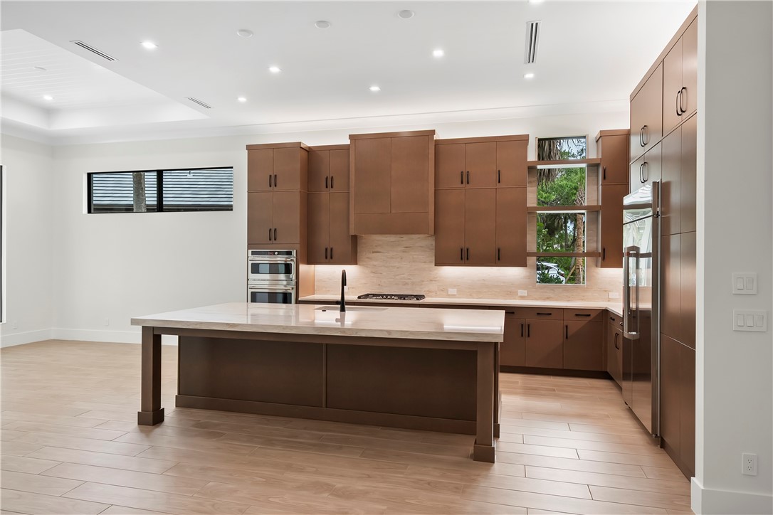 Kitchen featuring decorative backsplash, open shelves, light wood-type flooring, a kitchen island with sink, and recessed lighting