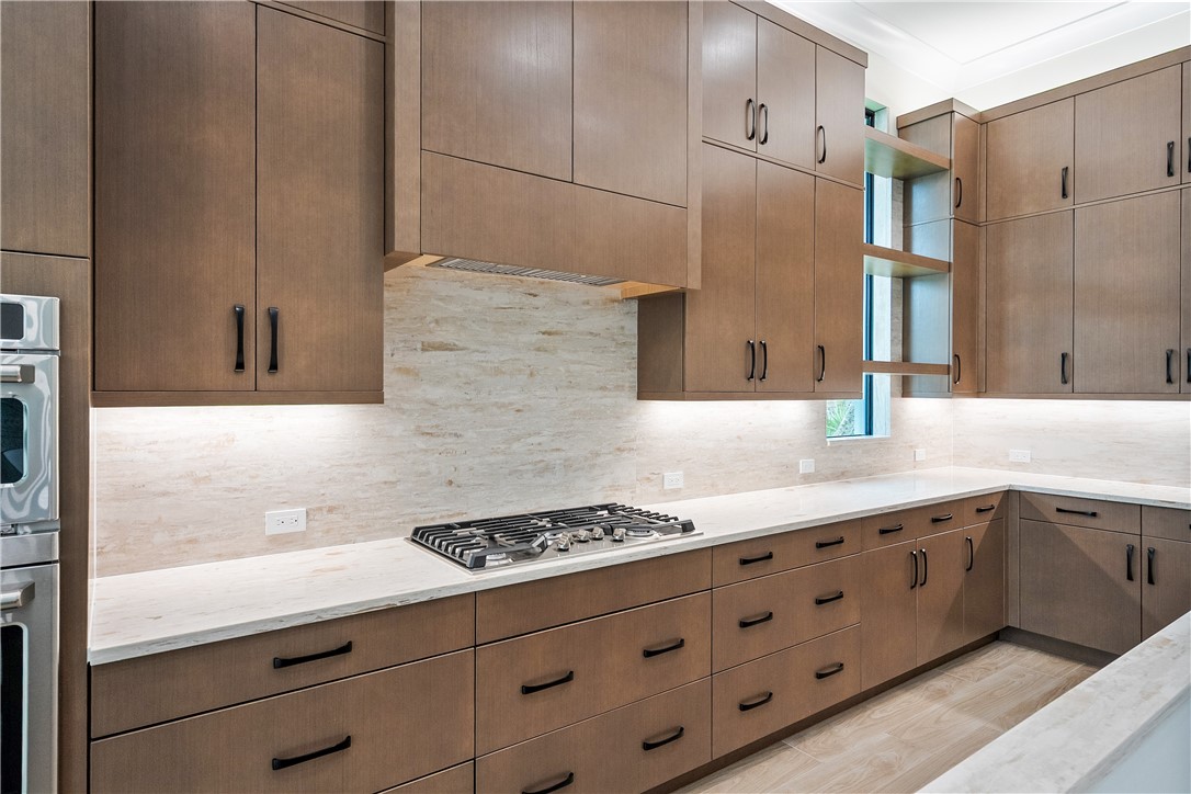 Kitchen featuring backsplash, light stone counters, light wood-style flooring, open shelves, and stainless steel appliances