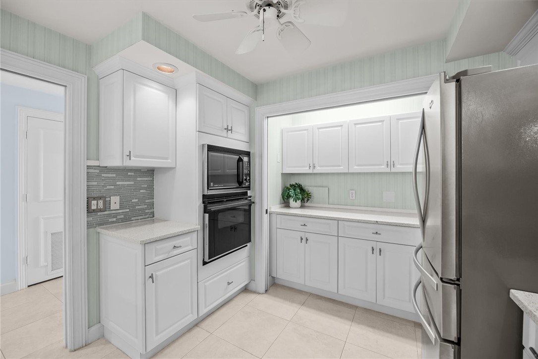 Kitchen featuring white cabinetry, built-in stainless steel appliances, stone countertops, and tile flooring