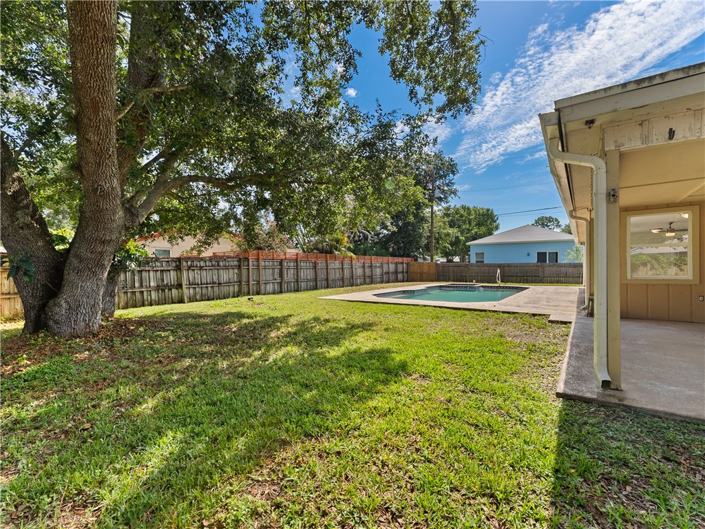 Expansive backyard featuring a mature tree, wooden privacy fence, inground swimming pool, and concrete patio