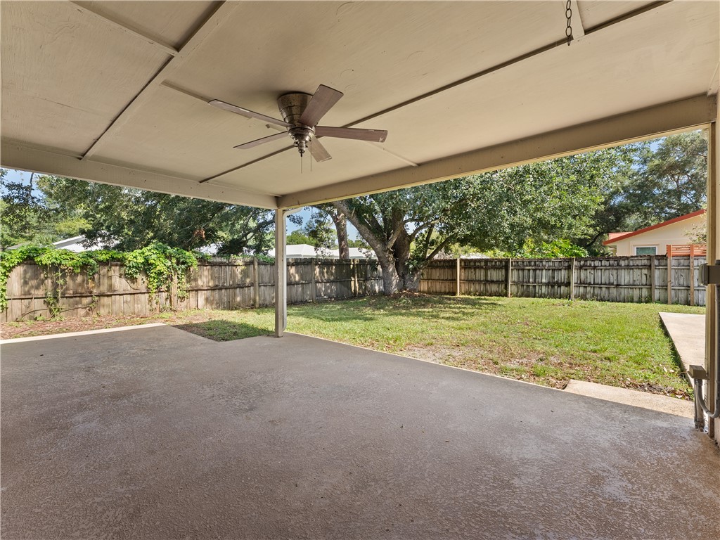 Covered patio with a ceiling fan, concrete flooring, and a spacious backyard featuring a wooden privacy fence and mature trees