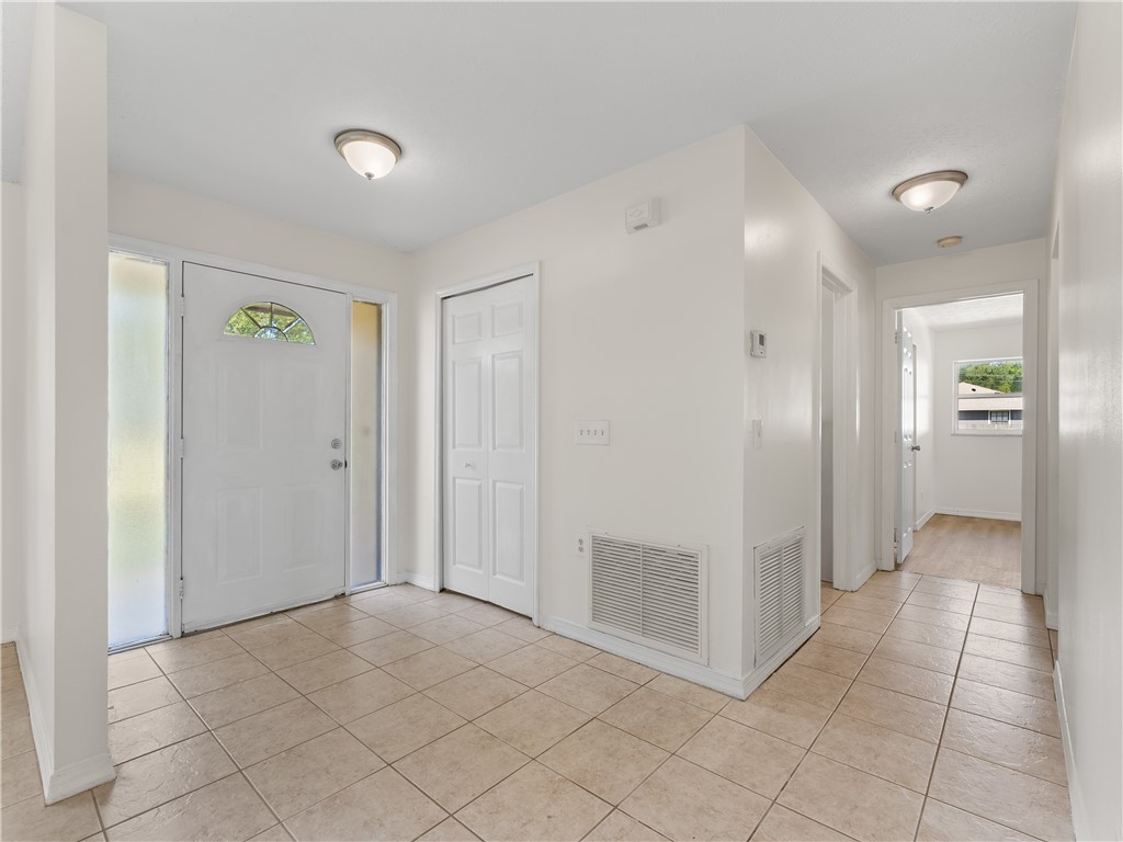 Entryway featuring ceramic tile flooring, a white paneled front door with an arched glass insert, and a hallway leading to interior spaces
