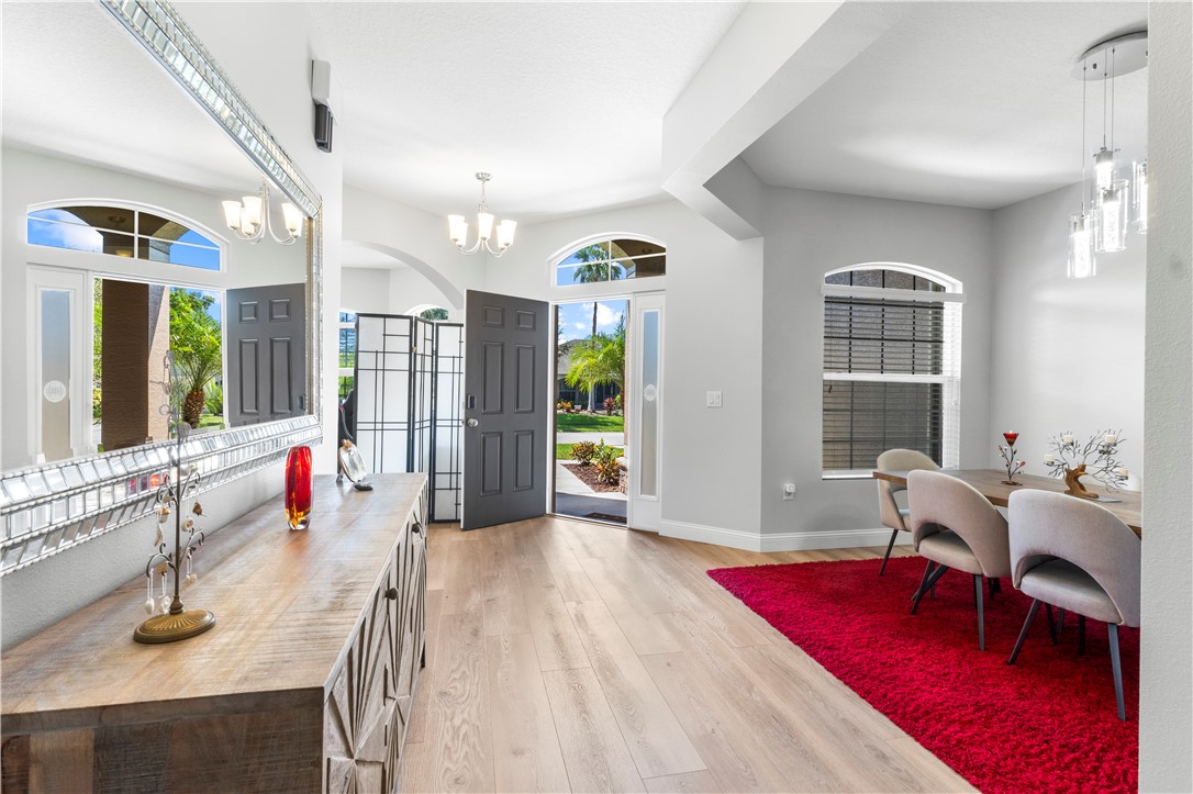 Light wood-finish flooring, arched doorways, a crystal chandelier, and a decorative console with an oversized mirror