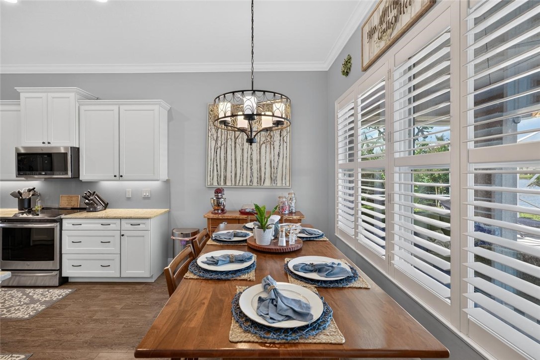 White cabinetry with stainless steel appliances, granite-style countertops, wood-finish flooring, and white plantation shutters