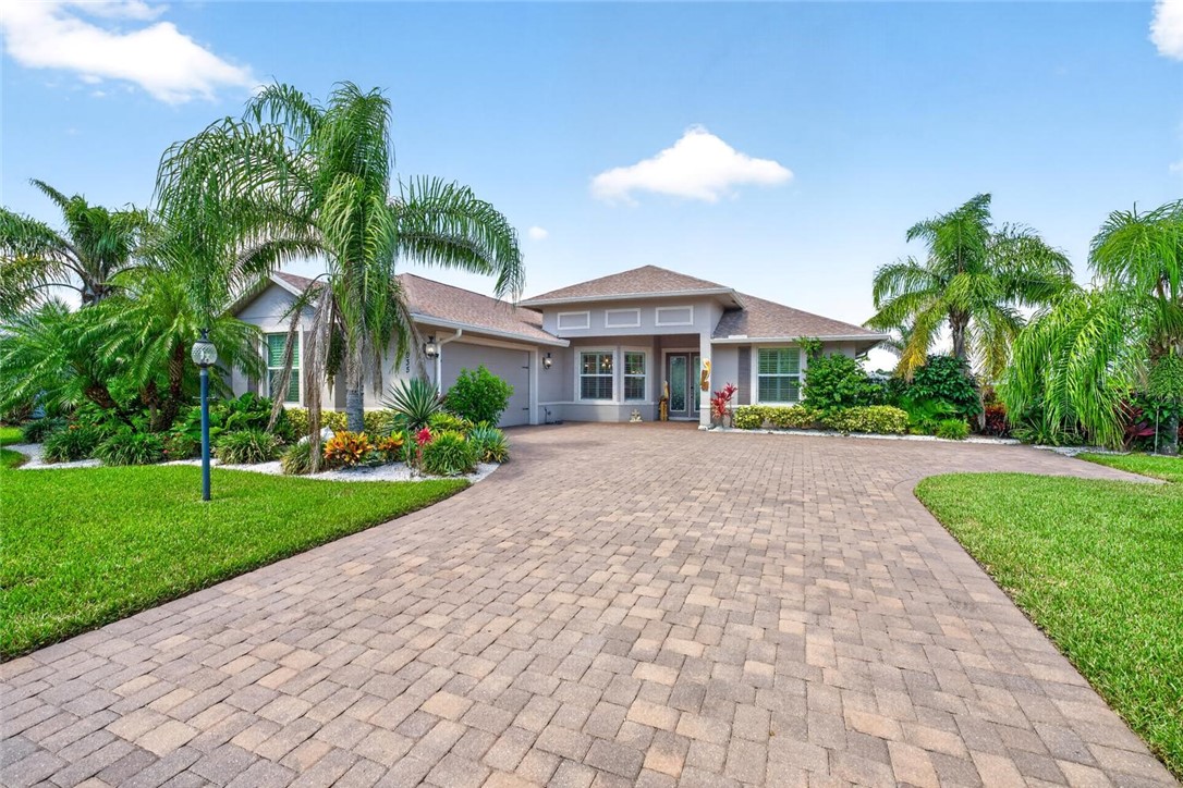 Expansive paver driveway with integrated walkways, mature tropical landscaping, and a well-maintained lawn