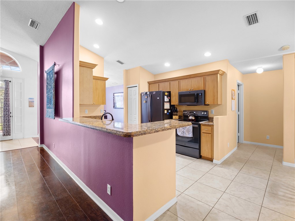 Kitchen featuring wood cabinetry, black appliances, granite-style countertops, and tile flooring