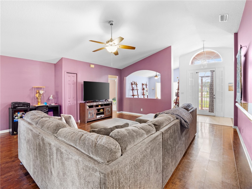 Vaulted ceiling with a ceiling fan, wood-finish flooring, interior arched doorway, and an entryway with a transom window