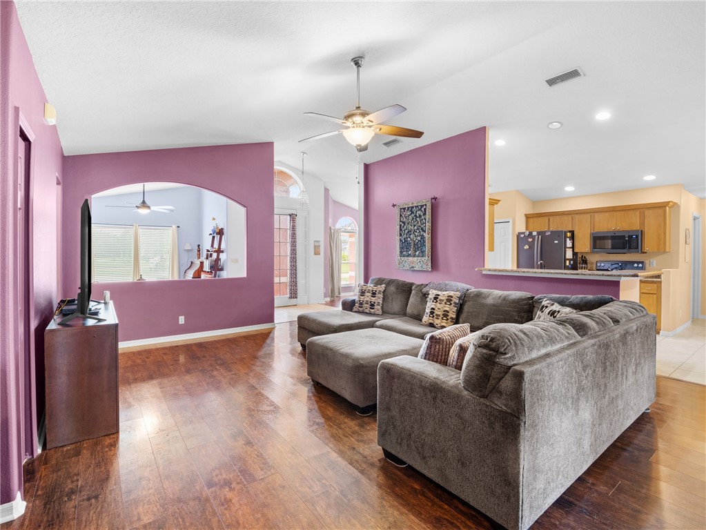 Vaulted ceiling, wood-finish flooring, recessed lighting, ceiling fan, and an arched interior pass-through