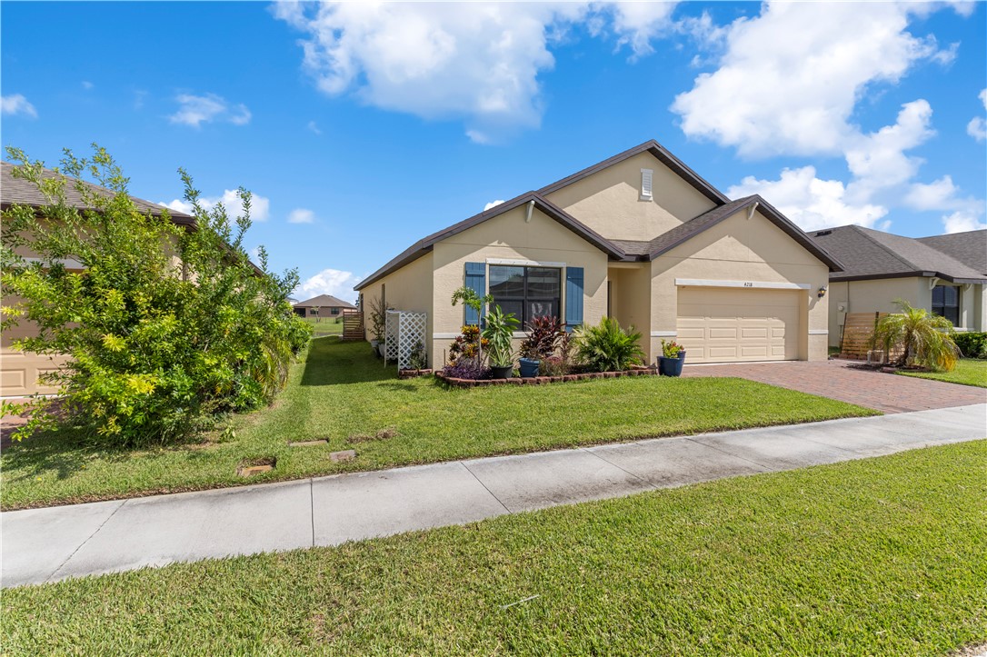 Single-story residence featuring a stucco exterior, an attached two-car garage, a paver driveway, and a well-maintained lawn with established landscaping