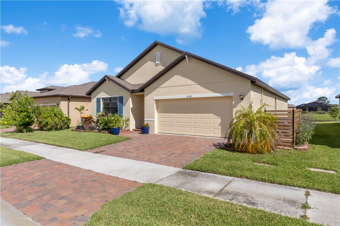 Stucco exterior with a shingle roof, paver driveway, attached garage, and decorative shutters