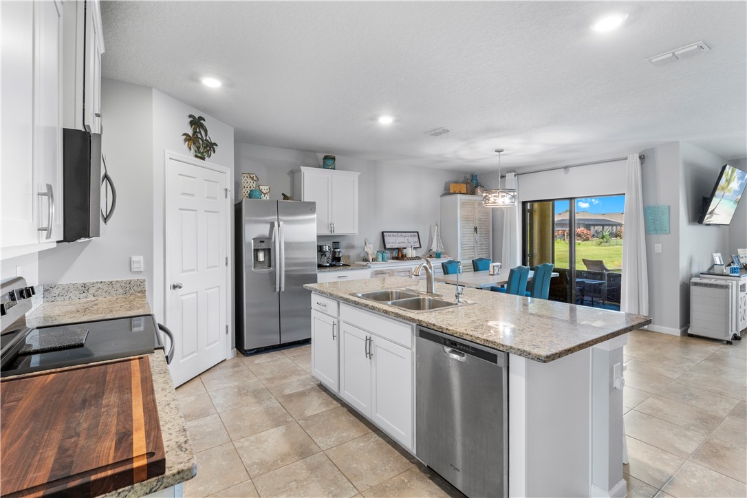 Kitchen featuring white cabinetry, light granite countertops, stainless steel appliances, a center island with double sink, and tiled flooring