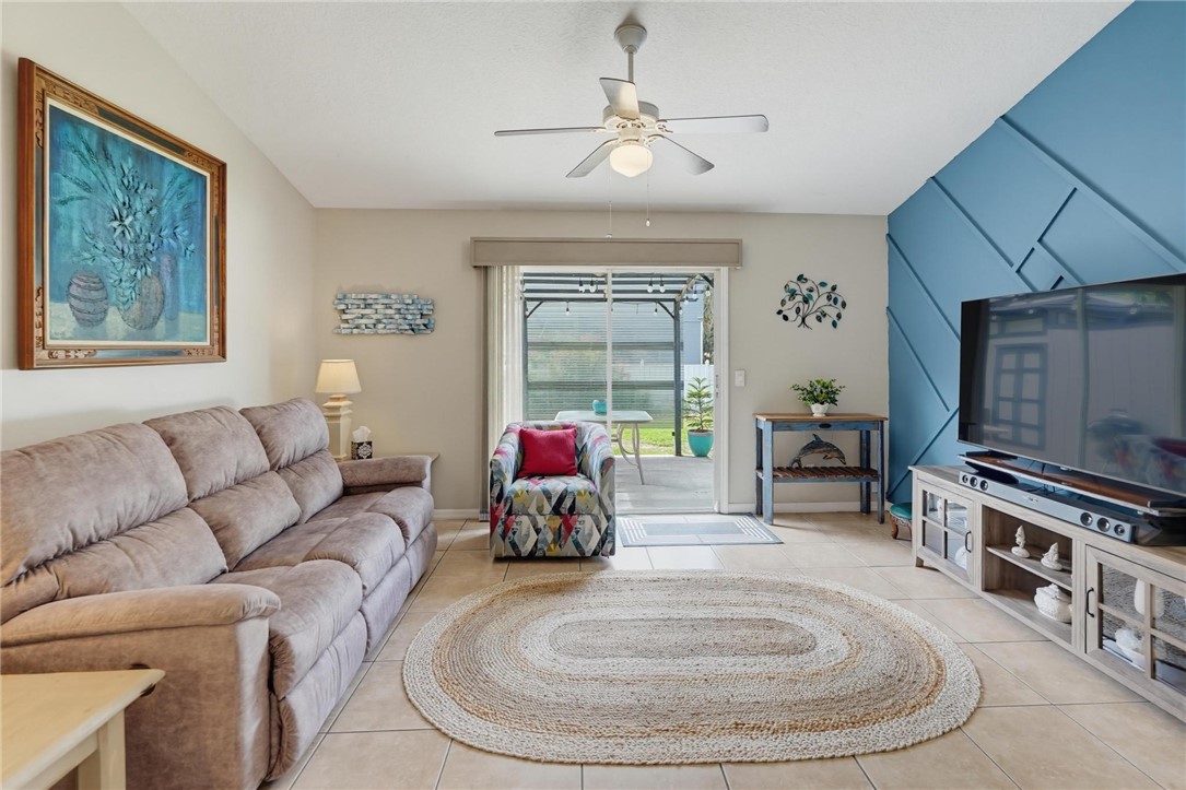 Tiled flooring throughout, ceiling fan with integrated lighting, built-in entertainment console, sliding glass doors, and a decorative accent wall