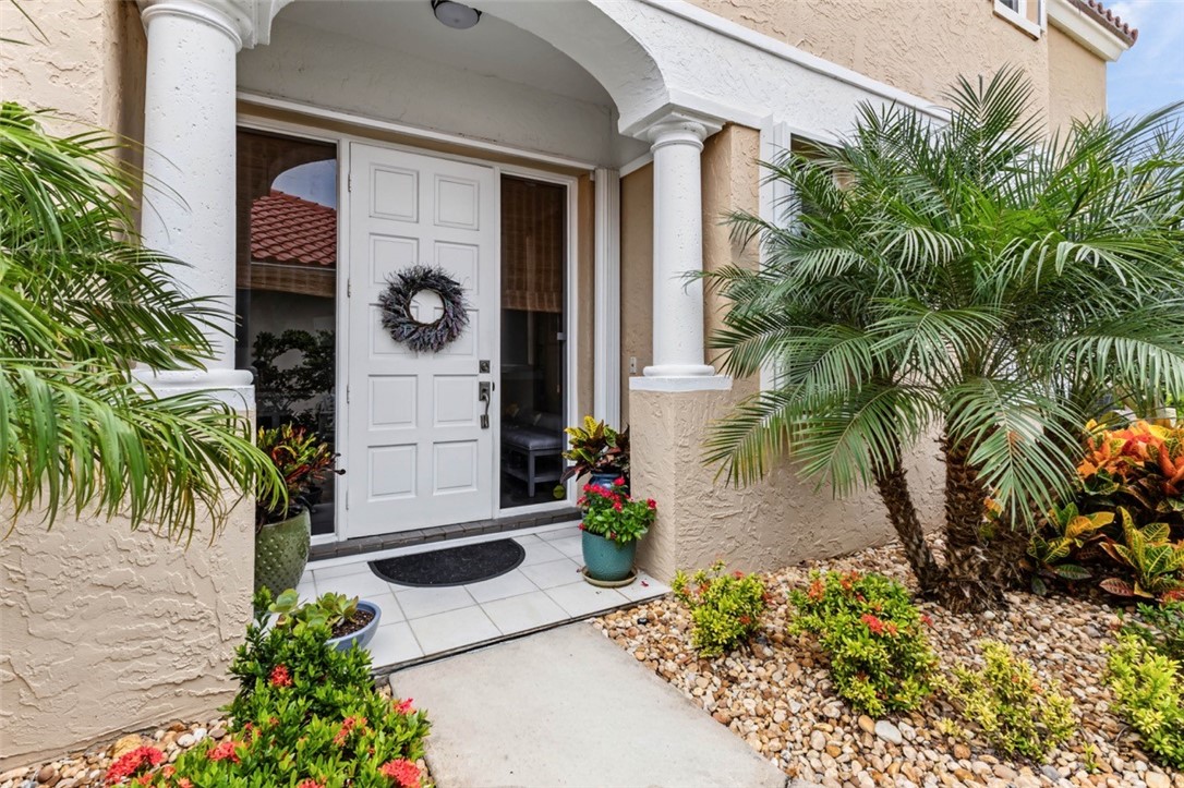 Portico entrance with decorative columns, white paneled entry door, tiled walkway, and landscaped rock garden