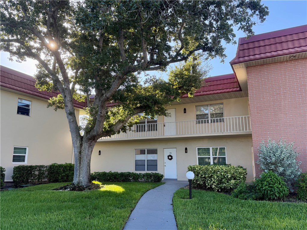 Two-story stucco building with a red tile roof, featuring a private balcony and a concrete pathway