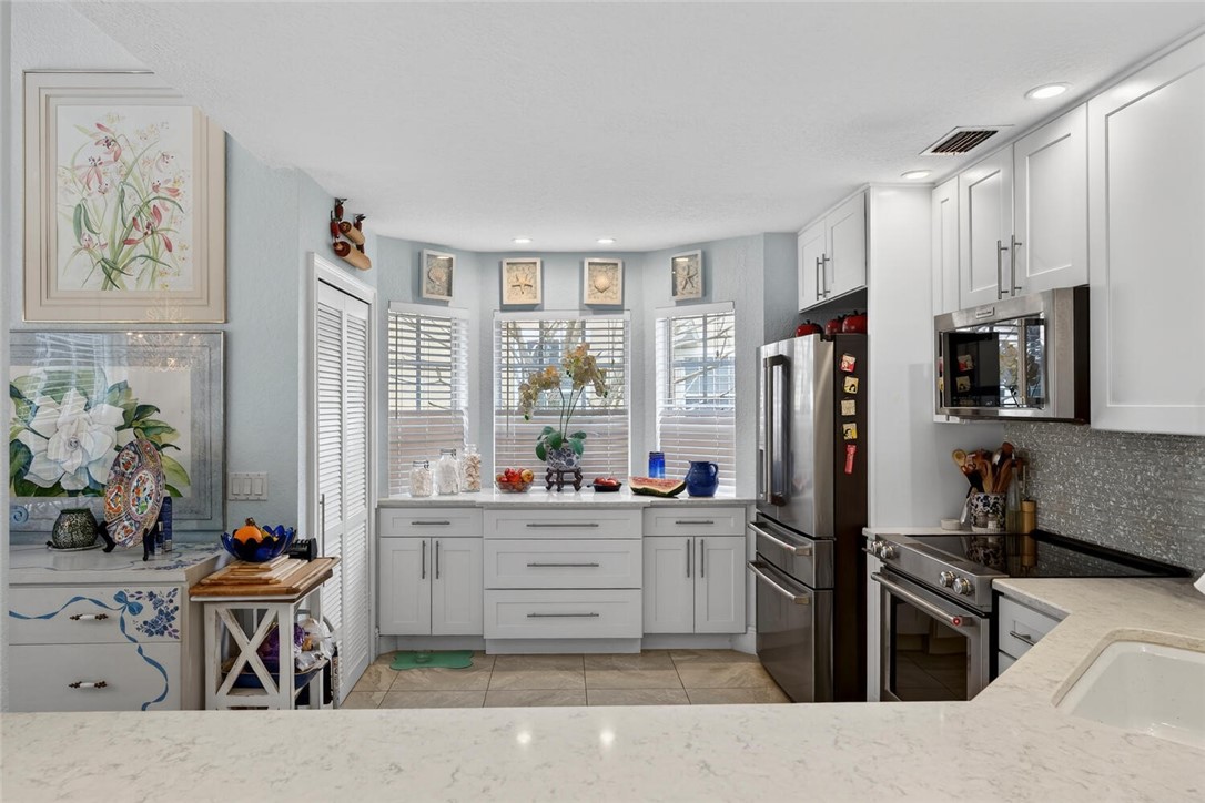 Kitchen featuring Kitchen Aid and GE Cafe appliances, custom white cabinets, bay window, quartz counters, recessed lighting and doors leading to walk-in customized pantry.