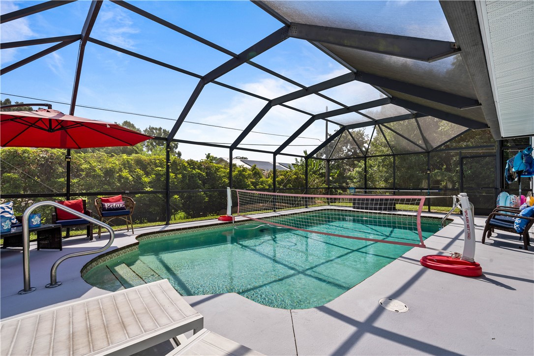 Screened-in pool enclosure featuring a pool with integrated steps, a tiled pool border, and a spacious concrete deck