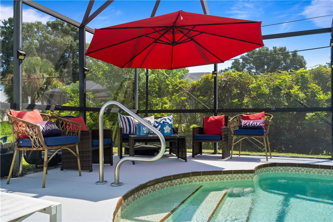 Screened outdoor living area featuring a pool with tiled steps, a poolside grab rail, and ample hardscaping