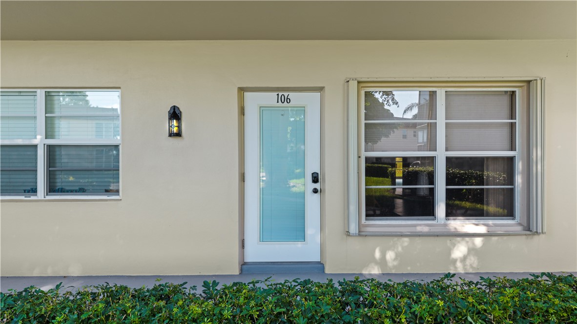 Stucco exterior featuring multiple windows, a light-colored entry door with a glass insert, and a wall-mounted lantern light fixture