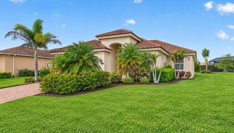 Stucco exterior with a terra cotta tile roof, paver driveway, mature palm trees, and manicured landscaping