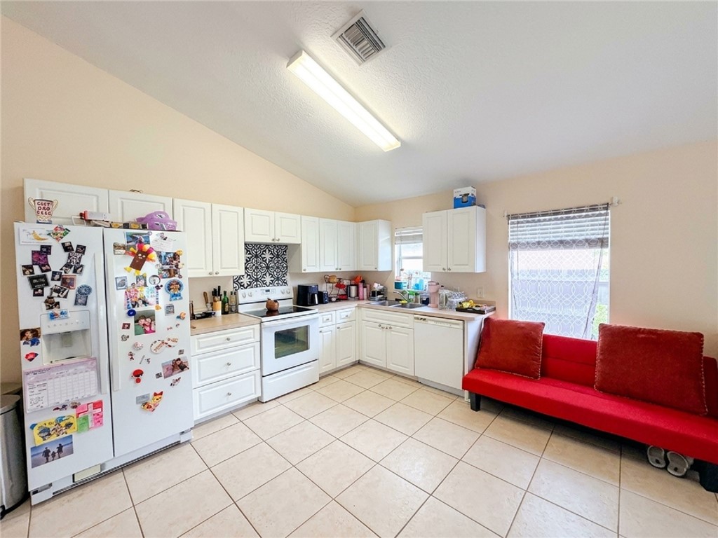 Vaulted ceiling kitchen featuring white cabinetry, a patterned tile backsplash, a built-in range, and square tile flooring
