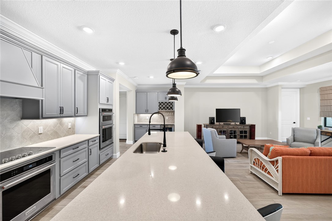 Open-concept kitchen featuring an oversized island, pendant lighting, stainless steel double ovens, and a built-in cooktop