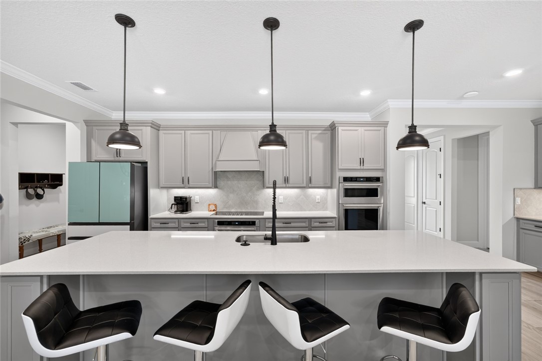 Expansive kitchen island with a built-in sink, gray shaker-style cabinetry, stainless steel appliances, and pendant lighting fixtures