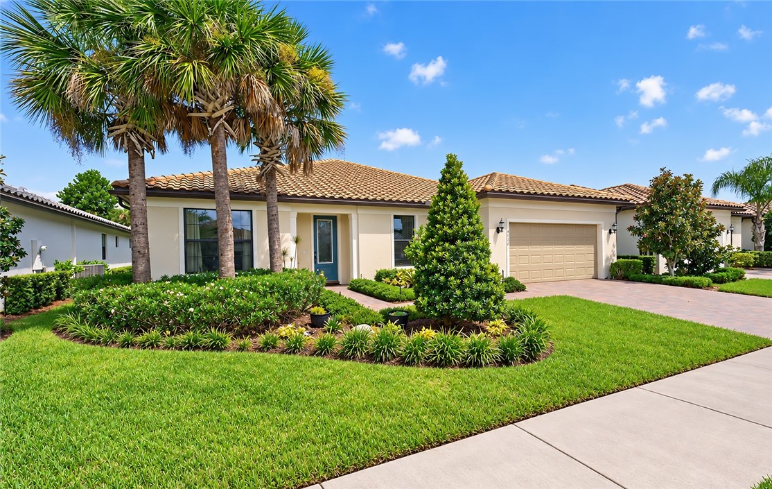 Stucco exterior with a tile roof, an integrated garage, a paver driveway, and mature landscaping