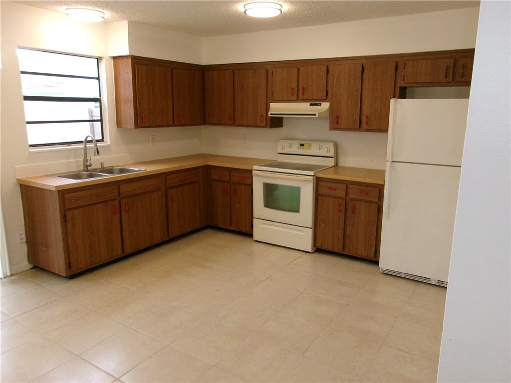 Kitchen featuring wood-finish cabinetry, a double basin stainless steel sink, tile flooring, and a white appliance package