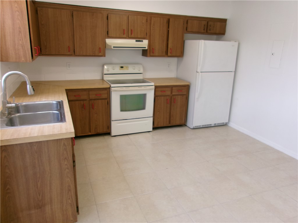 Wood-finish cabinetry, tile flooring, and white appliances including a refrigerator and range