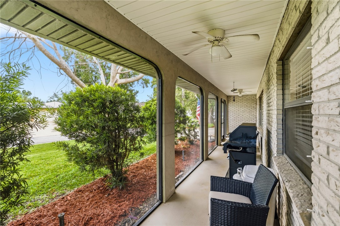 Screened porch featuring a textured concrete floor, multiple ceiling fans, and a light brick exterior wall